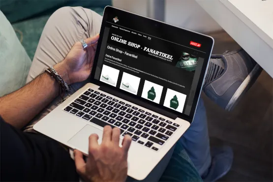 Hands operate a laptop displaying an online fan merchandise shop with product images.